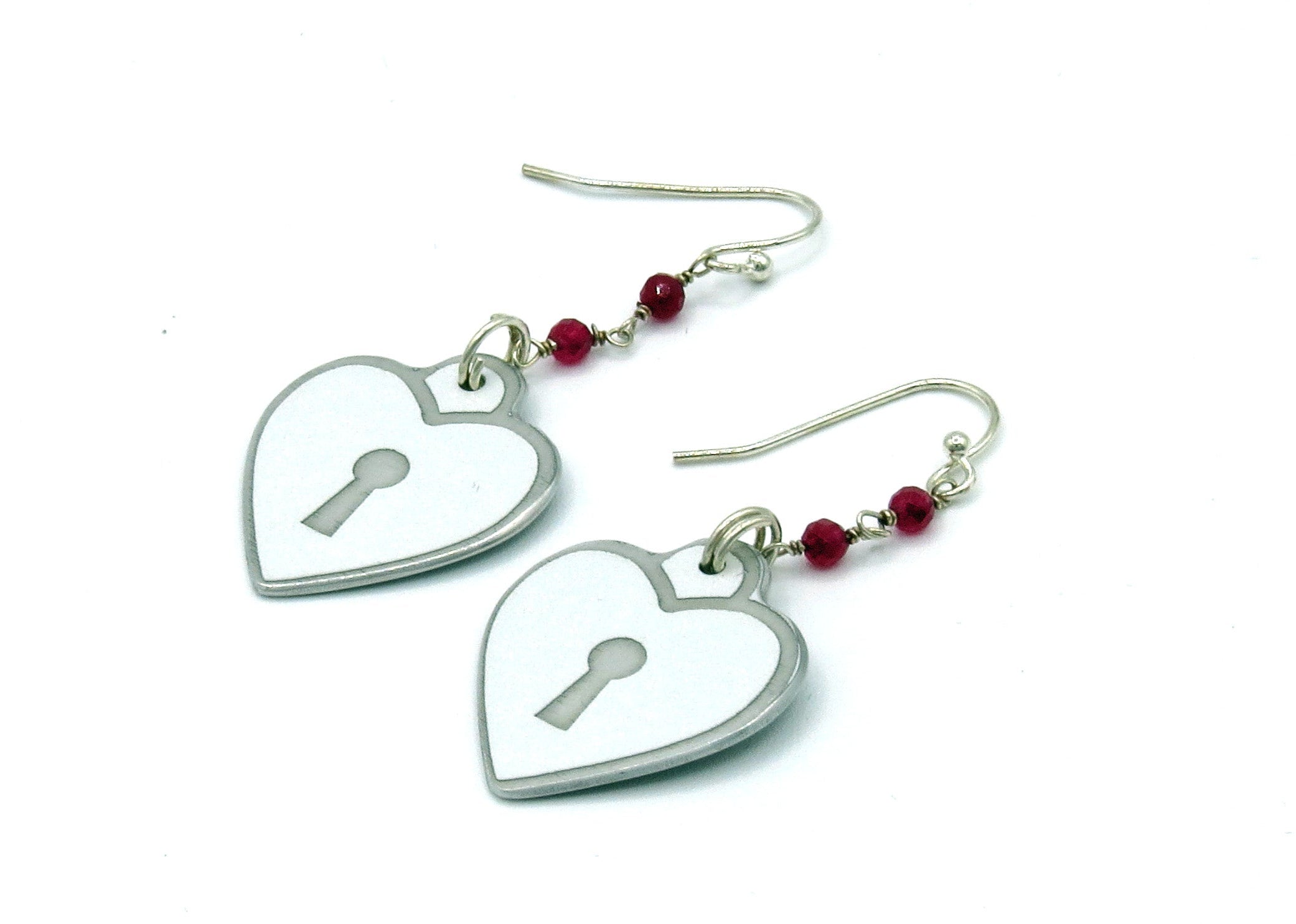 Heart-shaped earrings with key designs and red beads on a white background