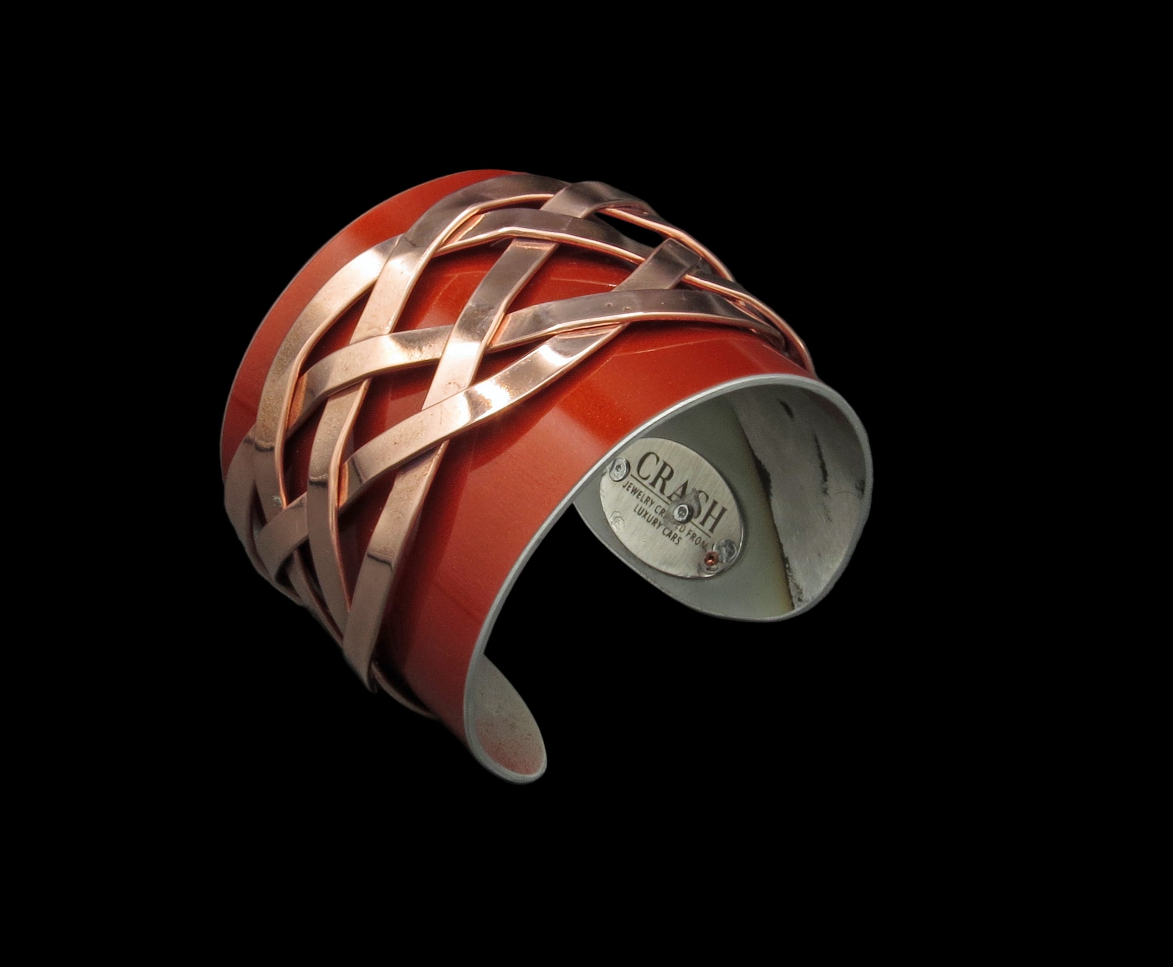 Cuff bracelet with red and copper braided design on a gray background