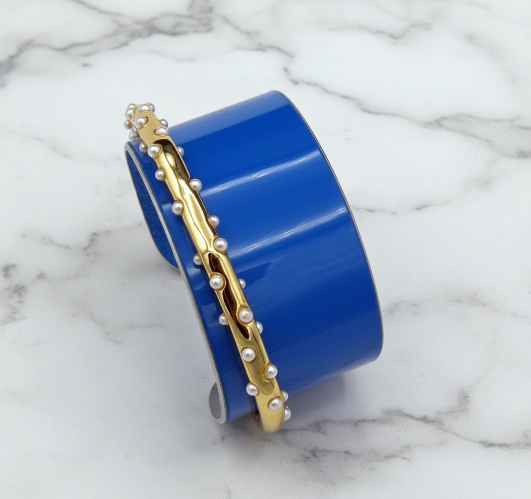 Blue cuff bracelet with gold band and pearl-like embellishments on a white background